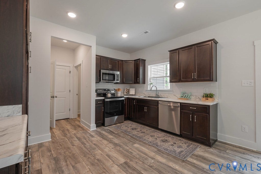 Kitchen featuring wood-finish flooring, dark wood cabinetry, stainless steel appliances, and white countertops