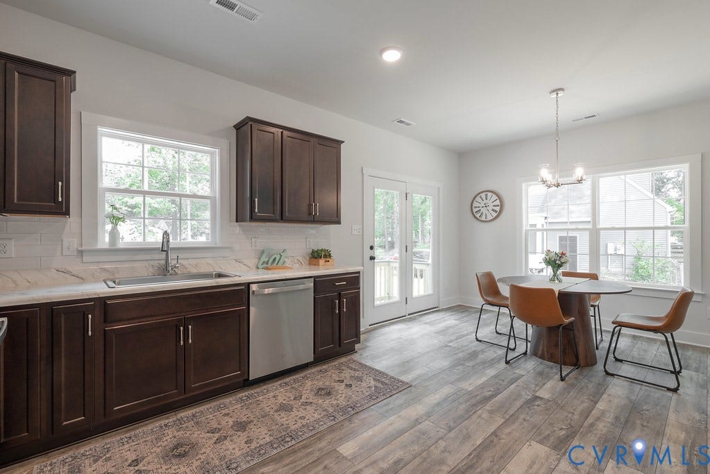 Dark wood-finish cabinetry with silver-tone hardware, white subway tile backsplash, stainless steel appliances, wood-finish flooring, and double French doors with transom windows