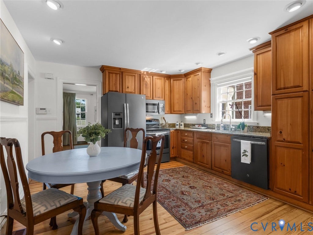 Kitchen featuring wood cabinetry, a stainless steel refrigerator, a black dishwasher, light-colored countertops, and hardwood flooring