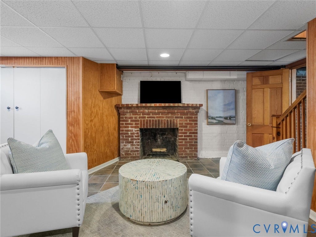 Brick fireplace with hearth, tile flooring, wood paneling, white built-in cabinetry, and wood staircase