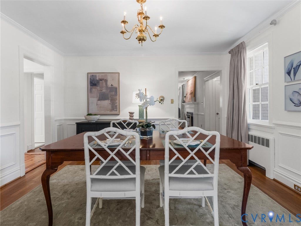 Hardwood flooring, wainscoting, crown molding, double-hung window, and a brass chandelier