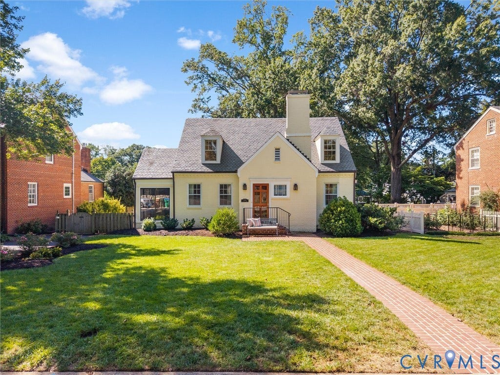 Gabled roofline, dormer windows, brick walkway, established landscaping, and a chimney feature