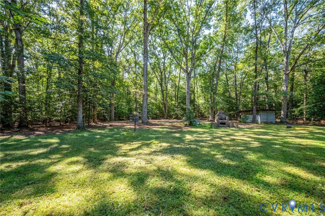 2409 Three Bridge Road, Rural, Powhatan, VA 23139 Expansive grassy area surrounded by mature trees, featuring a stone outdoor fireplace and a detached utility structure