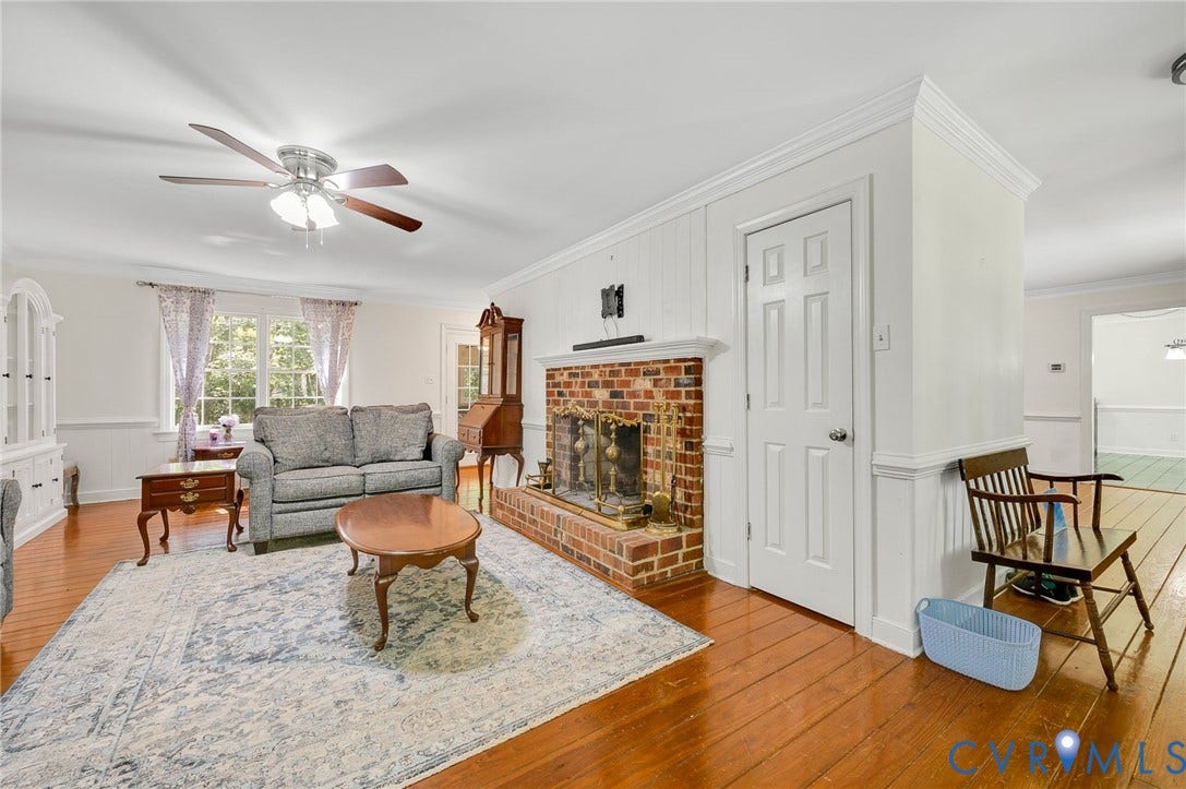 2409 Three Bridge Road, Rural, Powhatan, VA 23139 Brick fireplace with a metal grate, wood-finish flooring, white paneling, ceiling fan with light fixture, and crown molding