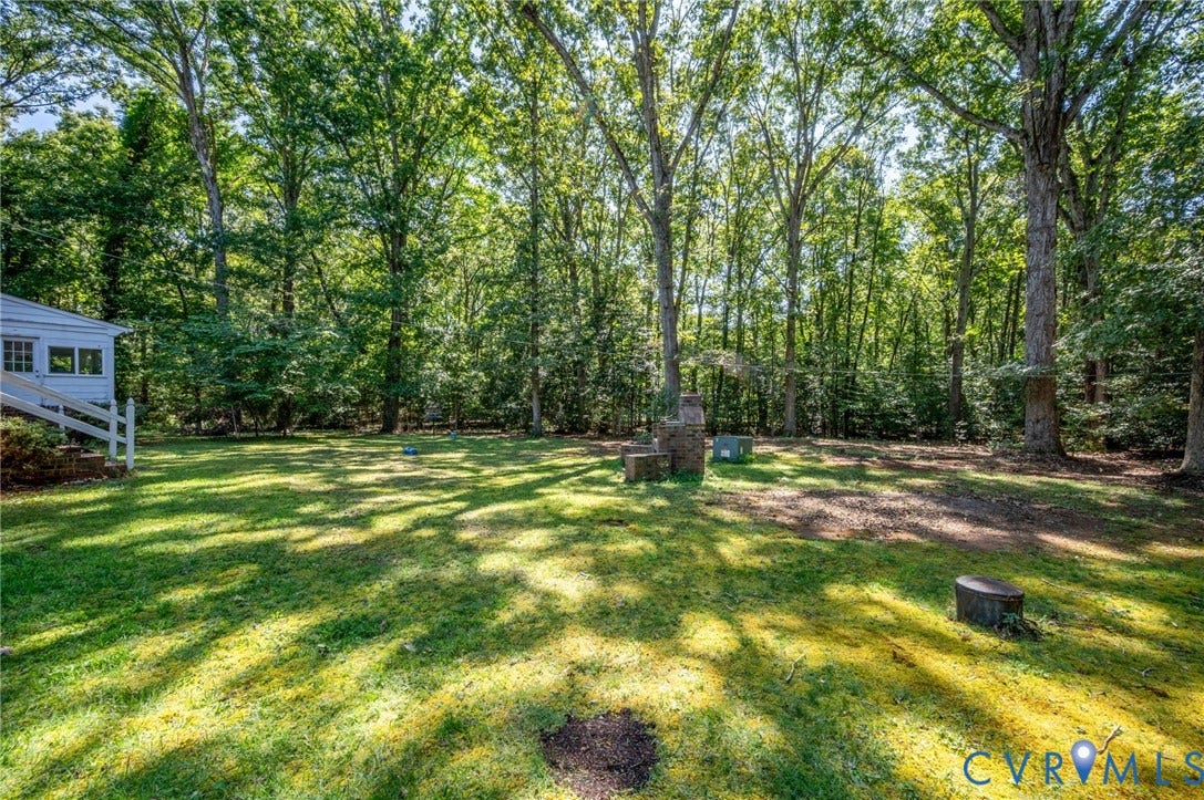 2409 Three Bridge Road, Rural, Powhatan, VA 23139 Expansive grassy backyard featuring mature trees, a built-in brick structure, and a white exterior building with railings