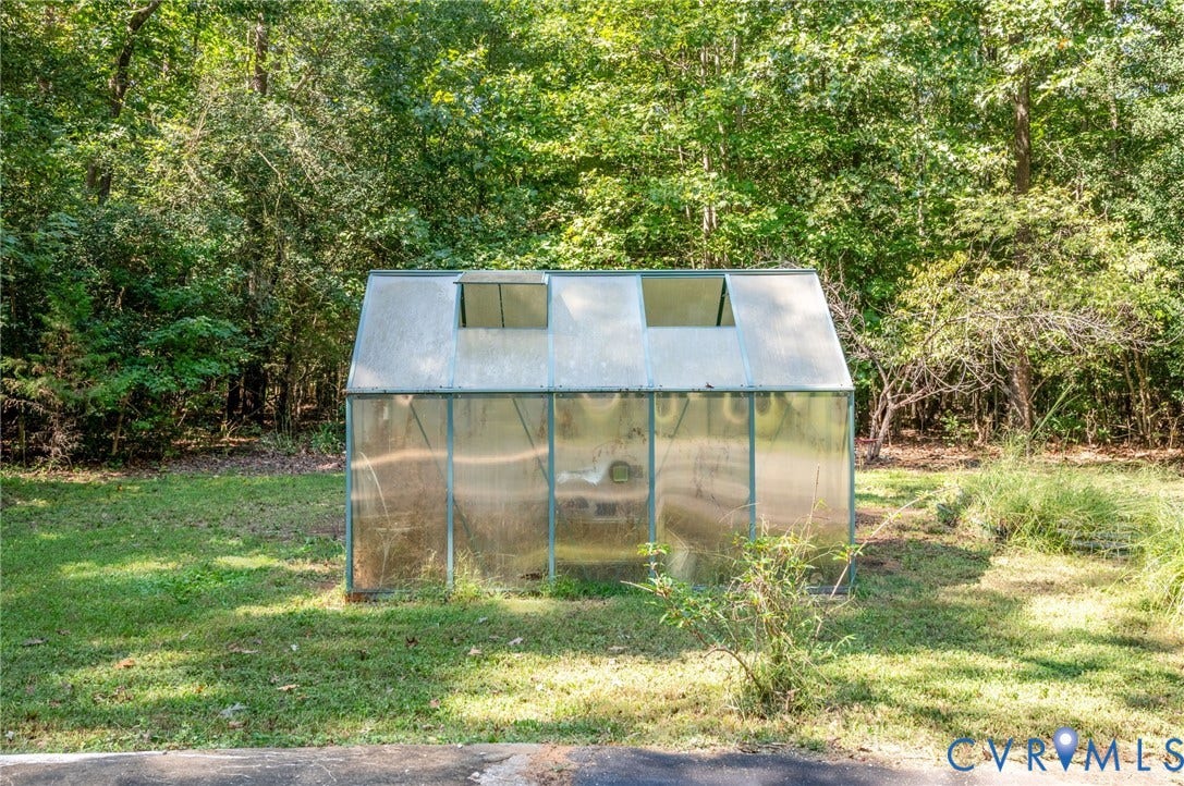 2409 Three Bridge Road, Rural, Powhatan, VA 23139 Freestanding greenhouse with a translucent panel construction and hinged roof vents, situated on a grassy area surrounded by mature trees