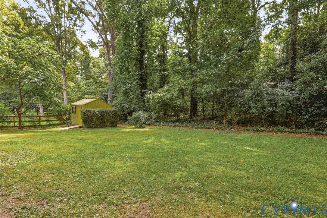 8349 Charlise Road, Oxford, Richmond, VA 23235 Expansive manicured lawn with mature trees, a wooden fence, and a storage shed with a hedgerow