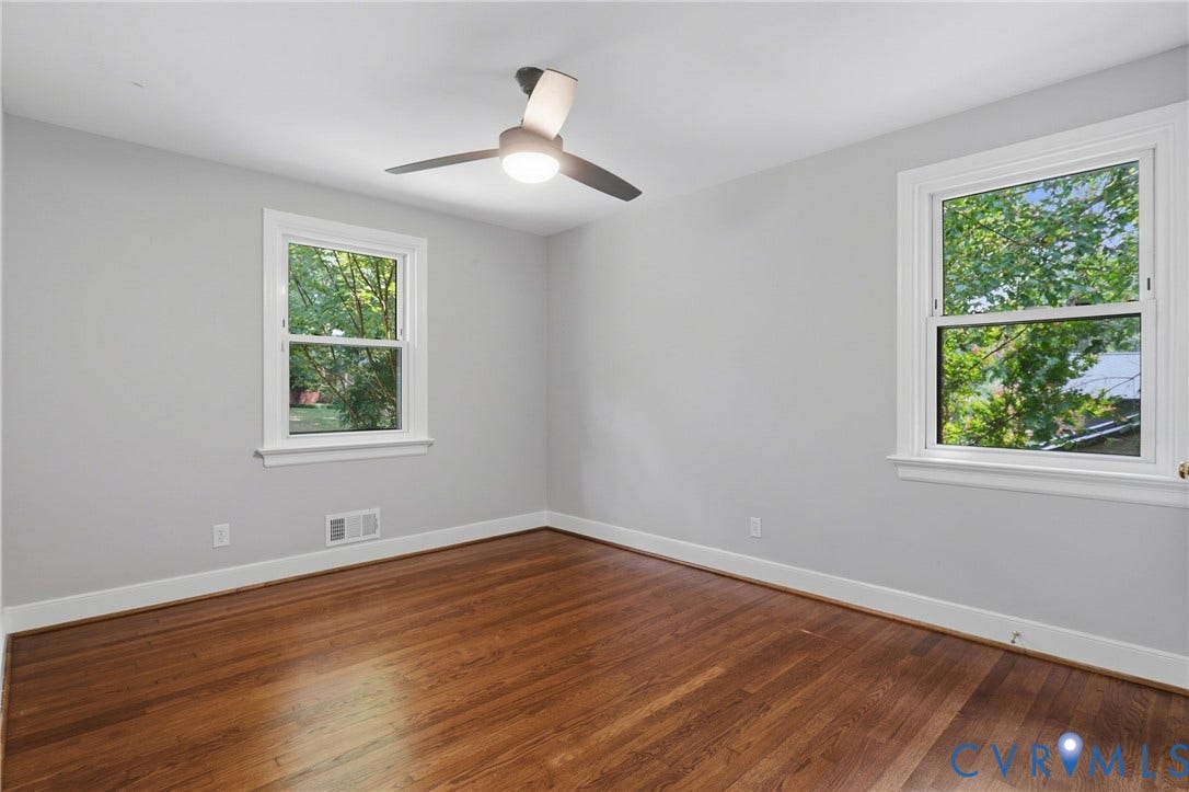 8349 Charlise Road, Oxford, Richmond, VA 23235 Hardwood flooring, two windows with white trim, a ceiling fan with integrated lighting, and light gray walls