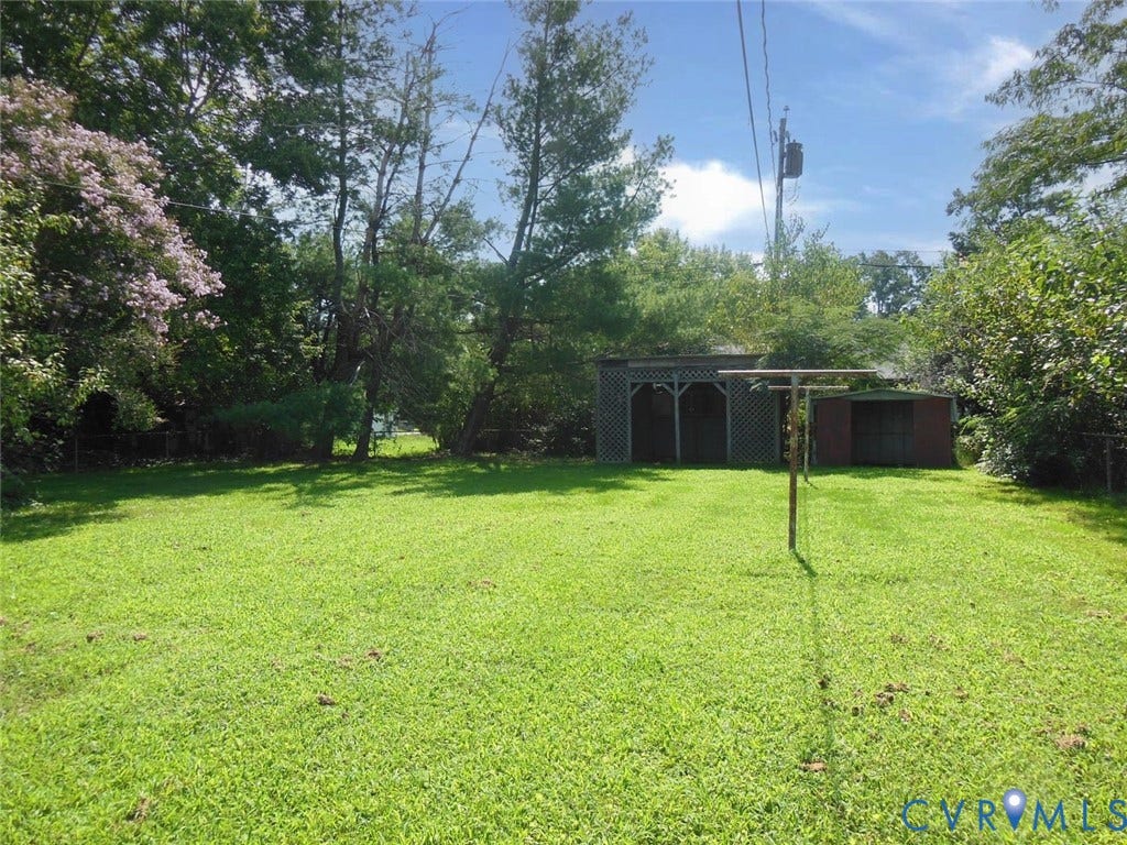 1805 Naselle Lane, Henrico, VA 23228 Expansive grassy yard area with mature trees, featuring a lattice-paneled shed and a secondary storage shed