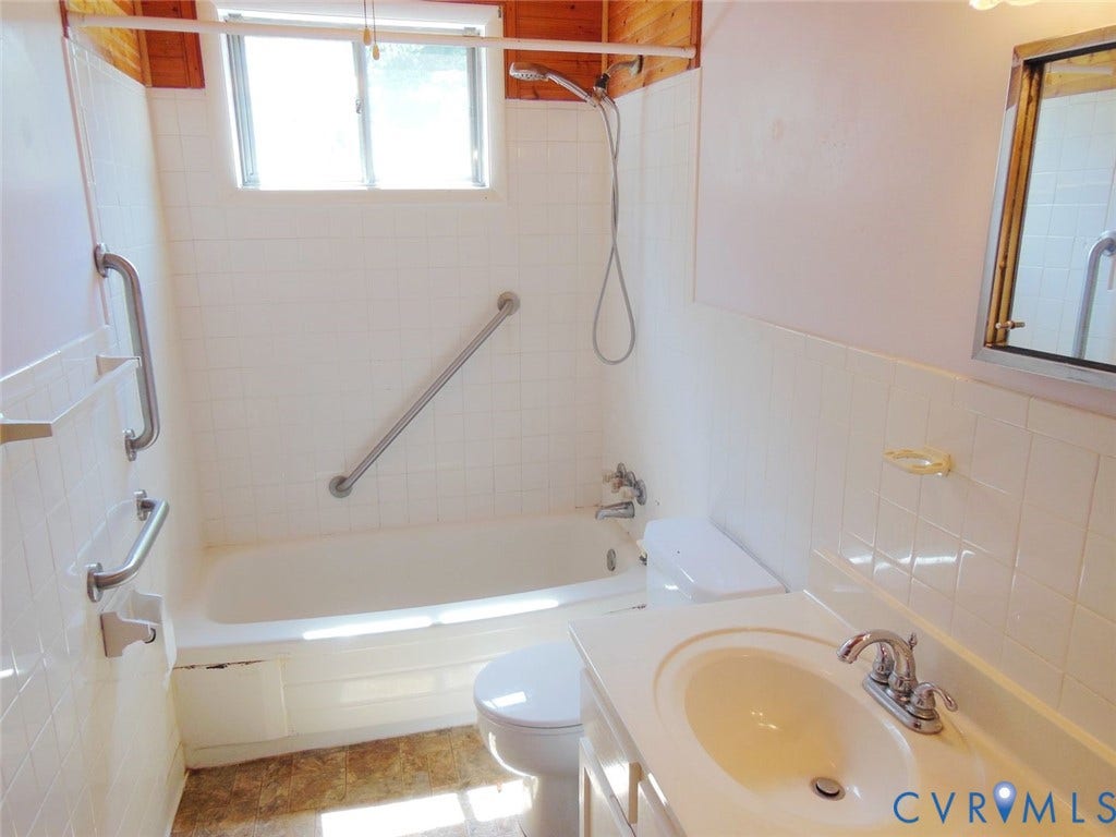 1805 Naselle Lane, Henrico, VA 23228 Hall Bathroom - White tiled bathroom featuring a single window, a bathtub with a showerhead, a toilet, a vanity with an integrated sink, and an embedded mirror