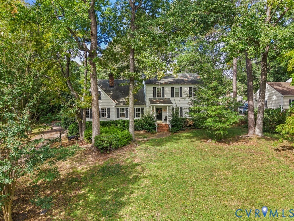 Traditional white siding exterior with dark shutters, front porch with brick steps, mature trees, and a spacious lawn
