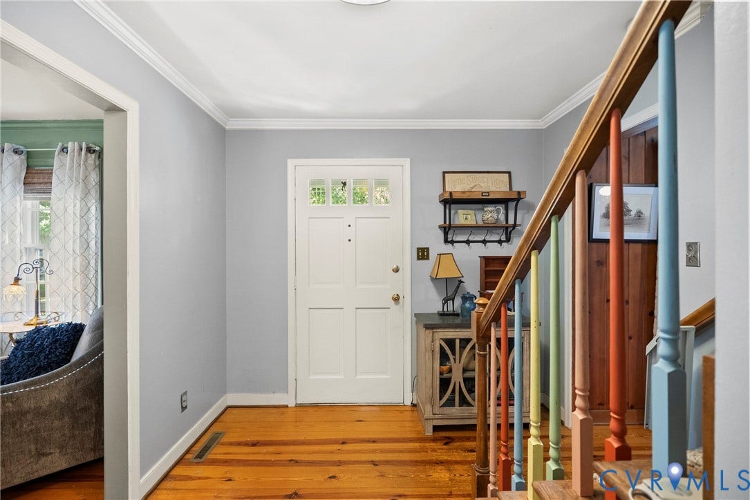 Wood-finish flooring, white paneled entry door with transom windows, crown molding, and a staircase featuring a wood handrail