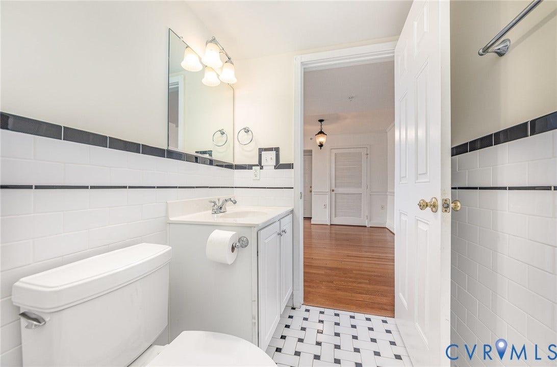 24 W Locke Lane, #1, Richmond, VA 23226 Bathroom featuring white subway tile walls with black trim, a vanity with a white countertop and integrated sink, a rectangular mirror, and a black and white mosaic tile floor