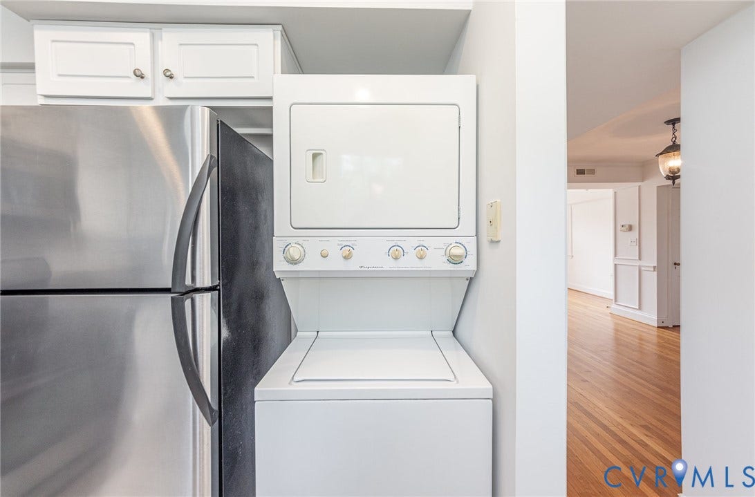 24 W Locke Lane, #1, Richmond, VA 23226 Stainless steel refrigerator, white stacked washer and dryer, white upper cabinetry with silver-tone hardware, and wood-finish flooring