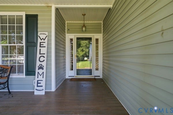 Covered front porch with wood-finish flooring, light-colored siding, dark-framed windows, and a glass-paneled entry door