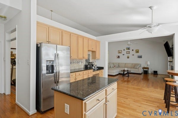 Kitchen featuring light wood cabinetry, stainless steel refrigerator, dark granite countertops, and wood-finish flooring