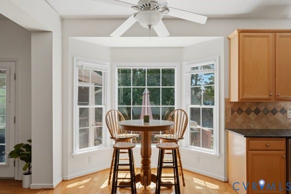 Bay window with multiple double-hung windows, wood-finish flooring, ceiling fan with light fixture, and kitchen cabinetry with a tile backsplash