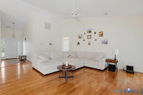 Vaulted ceilings with a ceiling fan, hardwood flooring, and a white entry door with a sidelight