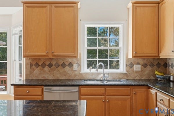 Wood-finish cabinetry, dark countertops, stainless steel sink with gooseneck faucet, tiled backsplash, and built-in dishwasher
