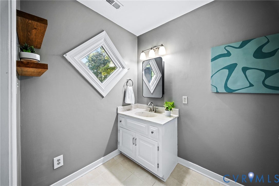 1608 Queens Point Drive, Henrico, VA 23238 White vanity with a stone countertop, integrated oval sink, diamond-shaped window, three-light fixture, and wall-mounted wooden shelving