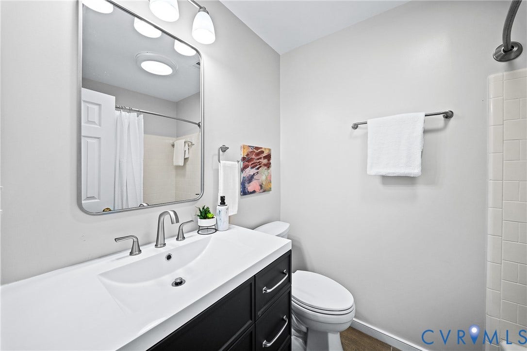 1608 Queens Point Drive, Henrico, VA 23238 Bathroom featuring a vanity with dark cabinetry and a white integrated sink, polished metal faucet, rectangular mirror with rounded corners, and a tiled shower surround
