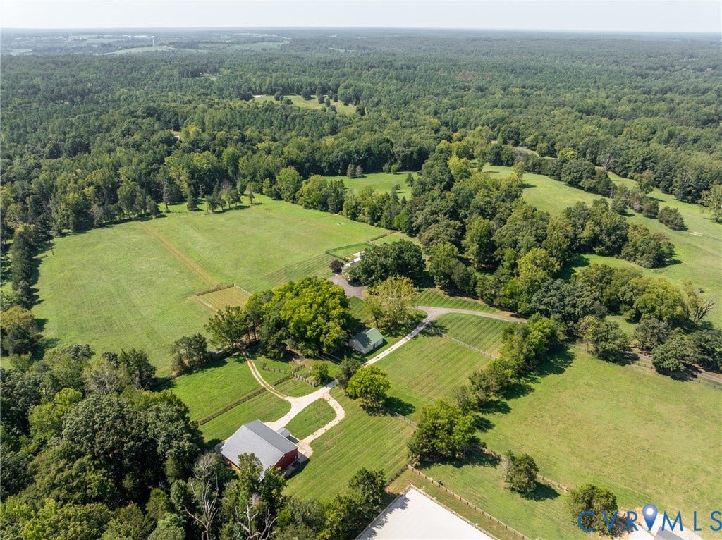 Expansive property featuring verdant fields, a mature treeline, a red barn, and a winding gravel driveway