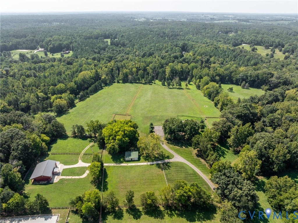 Expansive acreage featuring multiple open fields, mature tree lines, a red barn structure, a white-roofed dwelling, and unpaved driveways