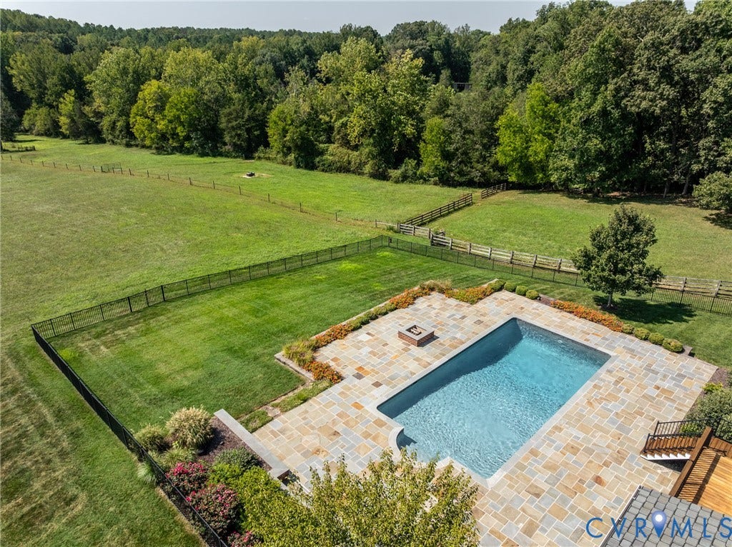 Expansive green space featuring a fenced swimming pool, natural stone patio, and varied landscaping