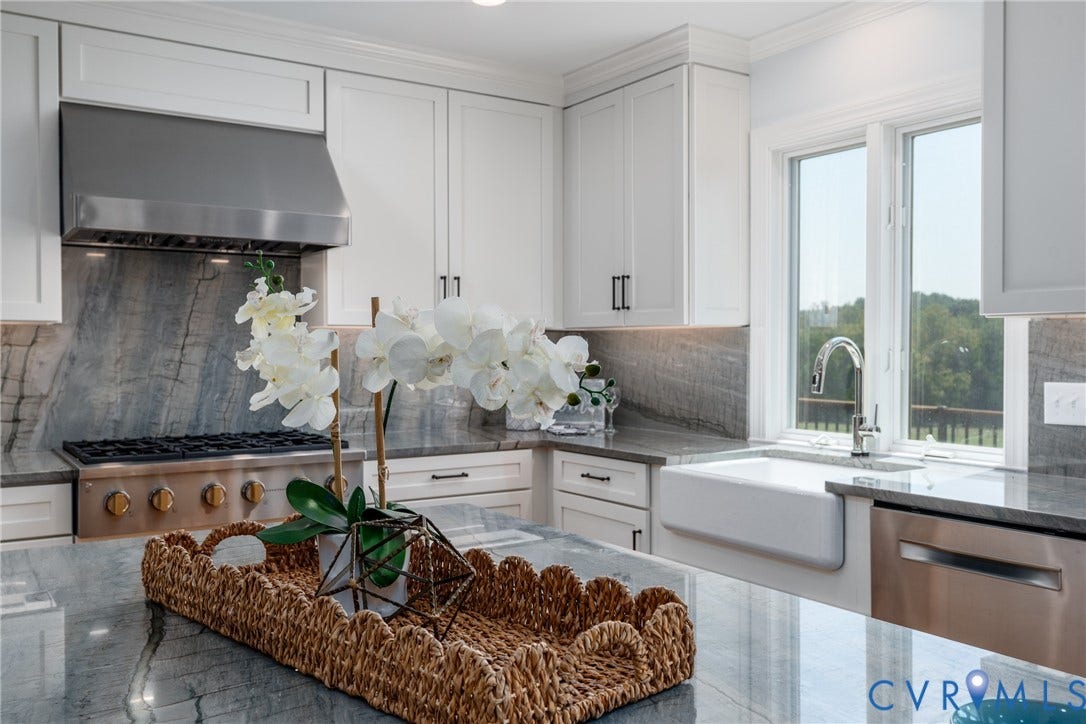 White shaker cabinetry with dark hardware, stone countertops with matching backsplash, stainless steel range hood, built-in gas range, and a white farmhouse sink