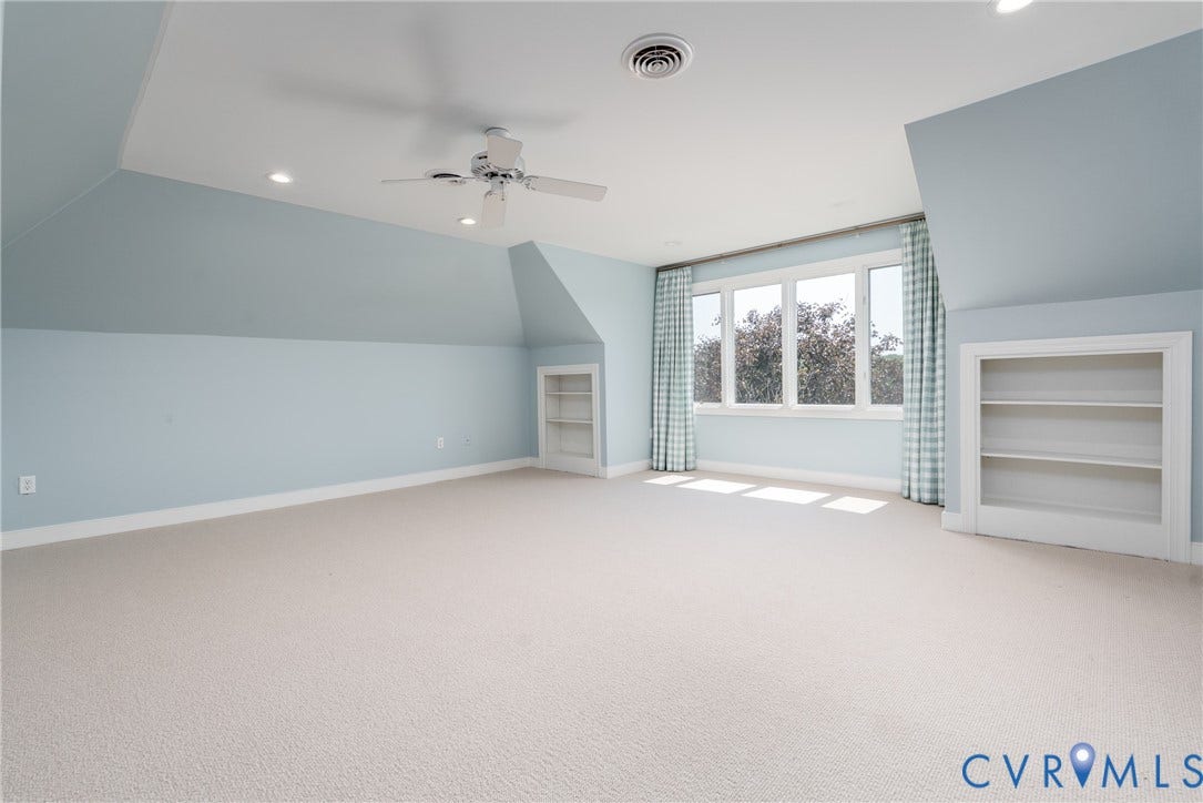 Spacious interior featuring a vaulted ceiling with recessed lighting, ceiling fan, carpeted flooring, built-in shelving, and multiple windows