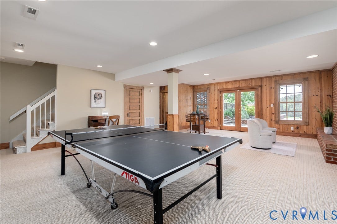 Recessed lighting, wood-paneled accent wall, French doors, brick fireplace, and carpeted flooring