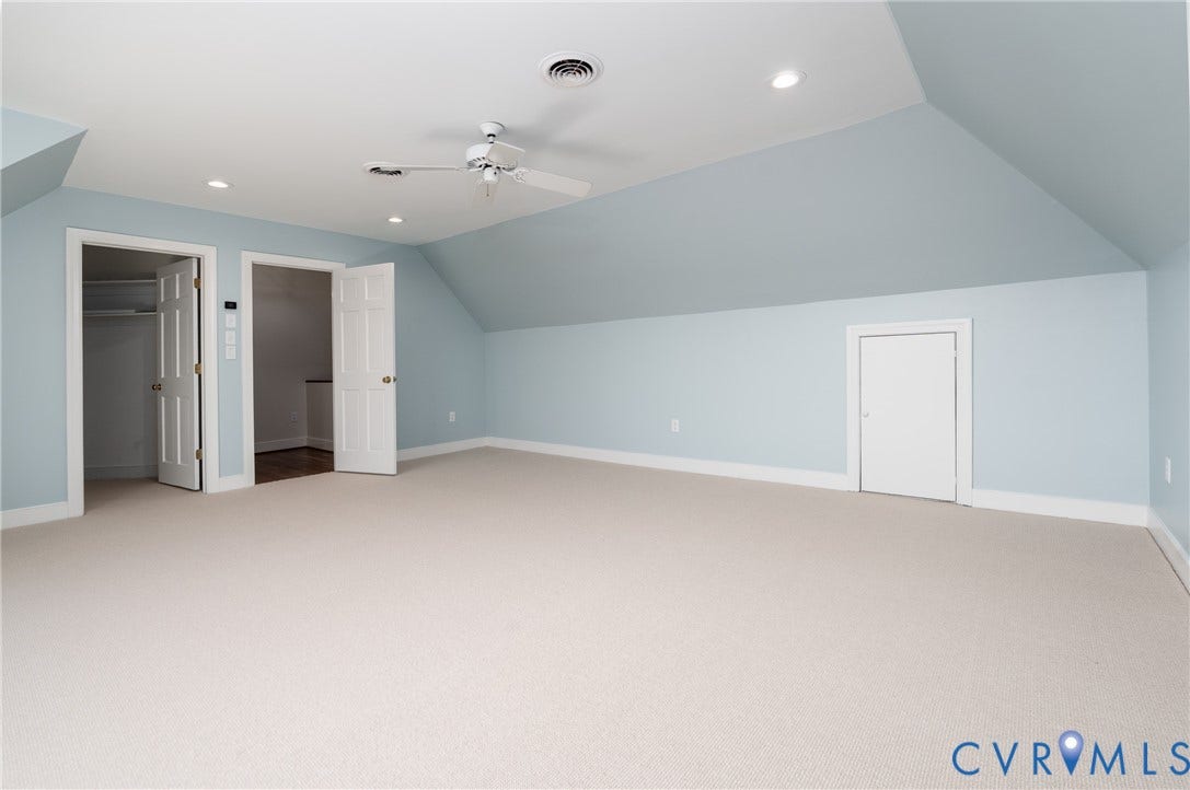 Expansive carpeted room featuring vaulted ceilings, recessed lighting, a ceiling fan, and multiple interior doors