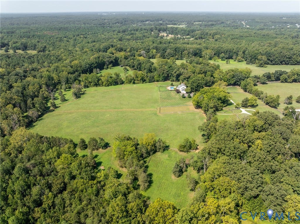 Expansive property featuring abundant mature trees, open grassy areas, a white-sided residence, and an in-ground pool