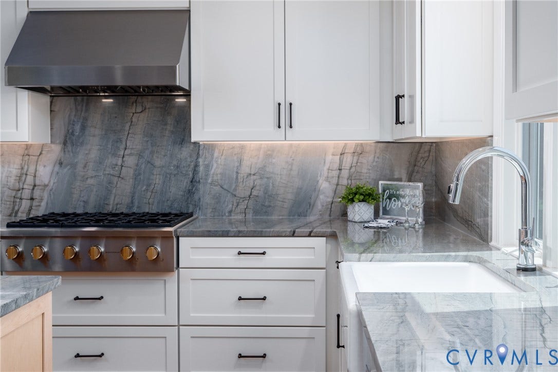 White shaker-style cabinetry, a stainless steel range hood, stone countertops with integrated backsplash, a chrome gooseneck faucet, and a large single-basin sink