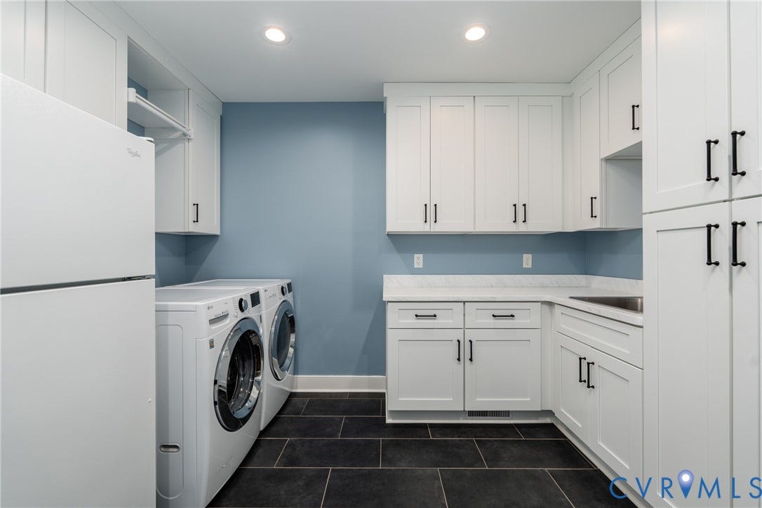White cabinetry with matte black hardware, dark rectangular floor tiles, light-colored countertops, and a built-in sink