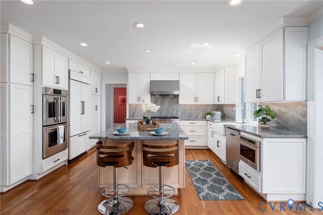 Kitchen featuring extensive white cabinetry, wood-finish flooring, a central island with countertop, stainless steel appliances, and integrated lighting
