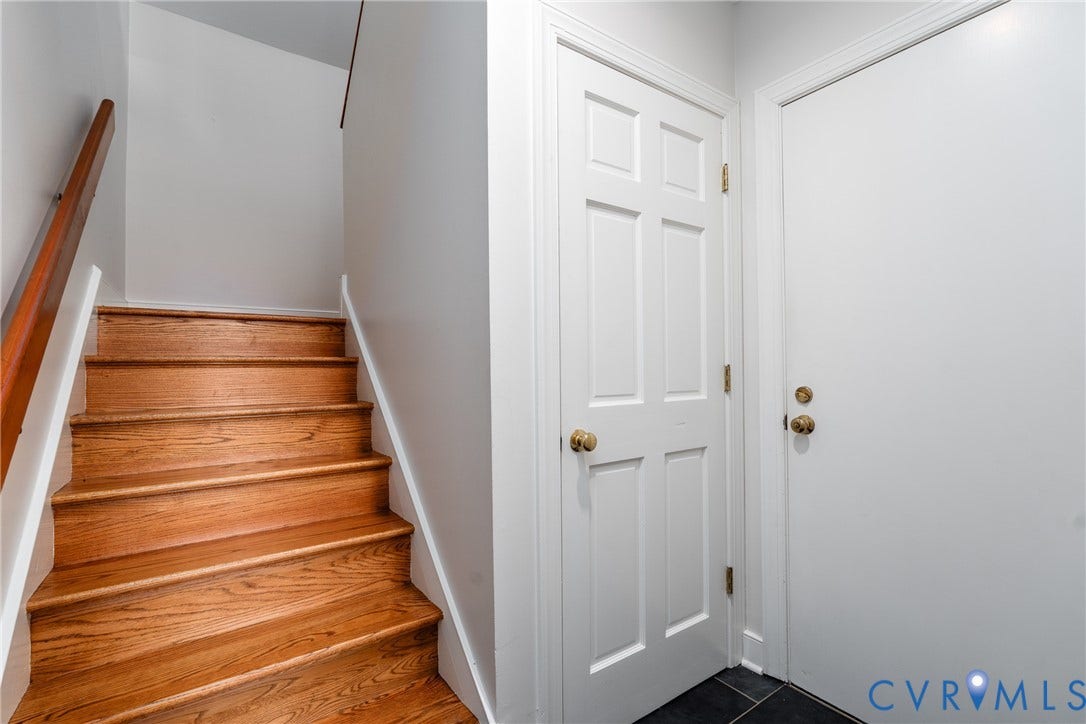 Hardwood staircase with a wood handrail, white risers, white trim, and a six-panel door