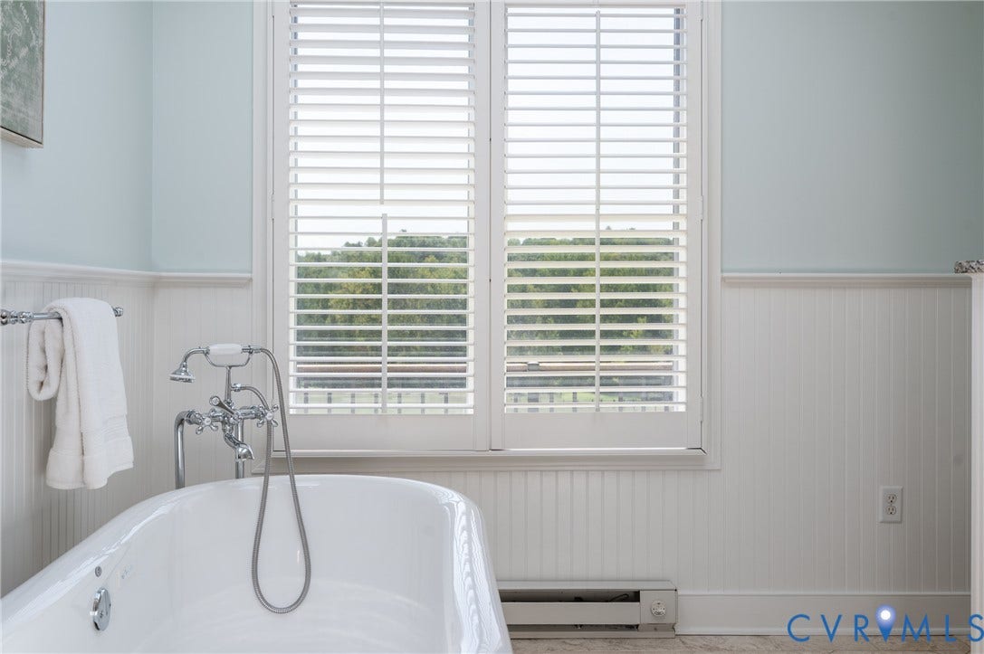 Freestanding bathtub featuring a chrome tub filler, full-height plantation shutters, and beadboard paneling