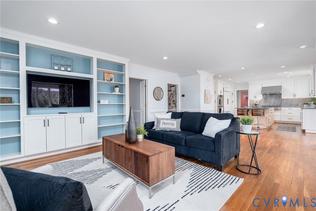 Built-in shelving and cabinetry with recessed lighting, hardwood flooring, and a kitchen featuring white cabinetry, stainless steel appliances, and stone countertops