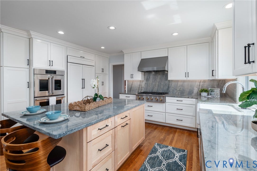 Gourmet kitchen featuring white cabinetry, stainless steel appliances, a center island with seating, and wood-finish flooring