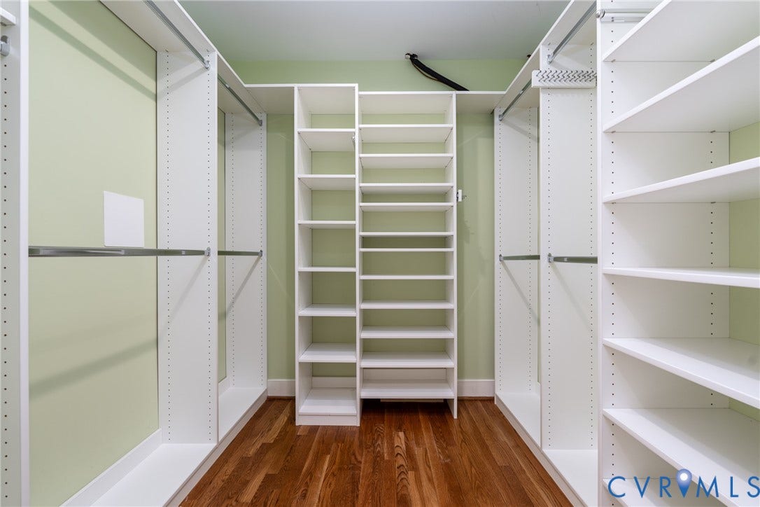 Built-in closet system featuring white shelving, multiple hanging rods, and wood-finish flooring