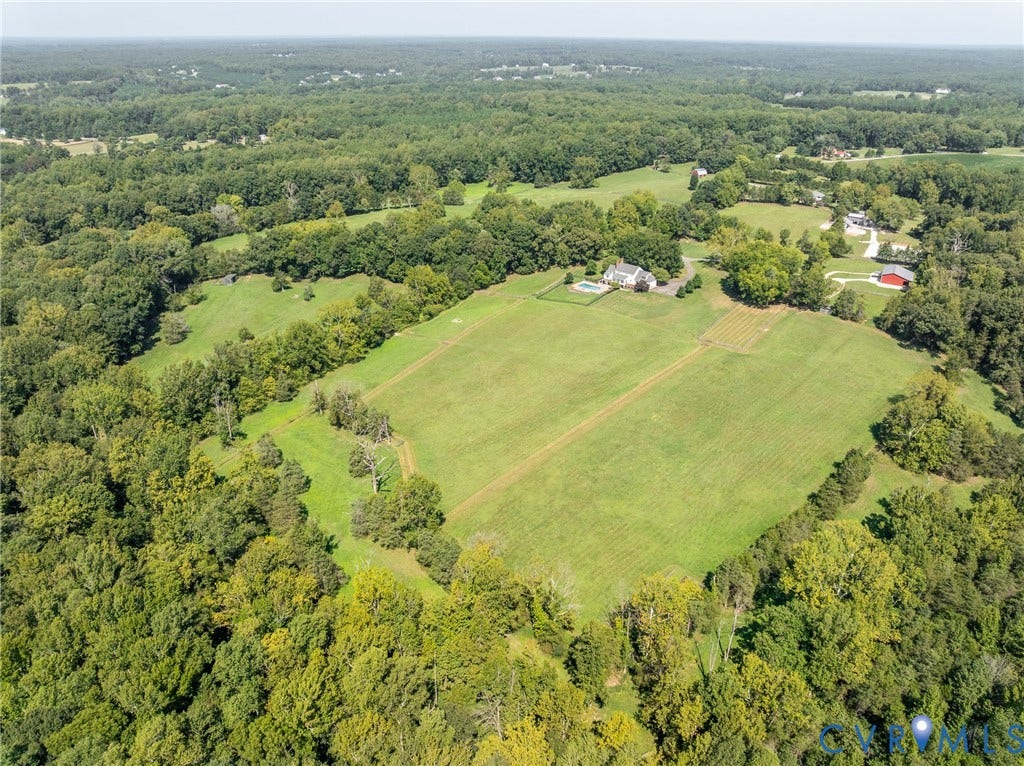 Expansive property featuring a residence, detached red barn, swimming pool, and extensive green space surrounded by mature trees