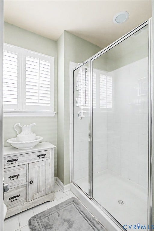 Primary En-Suite Bath Featuring Glass-Enclosed Shower, Tile Flooring, Plantation Shutters, and Distressed Wood Vanity.