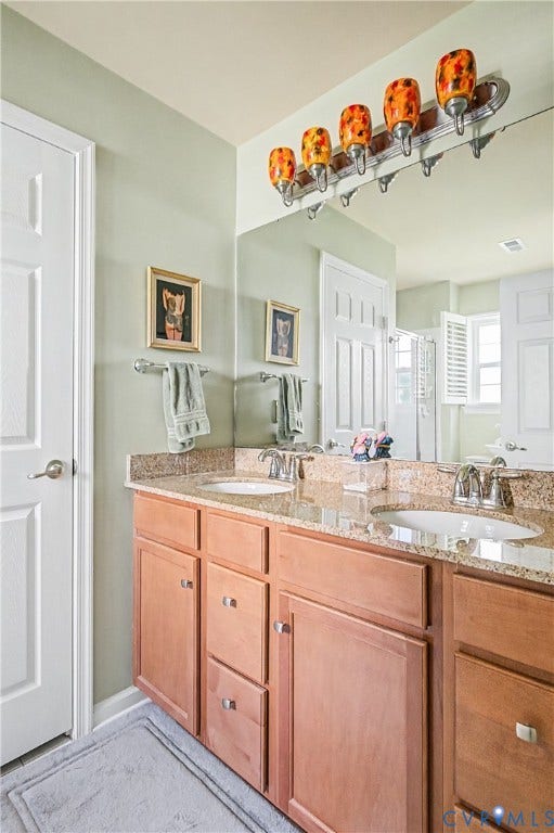 Primary En-Suite Bath Featuring Dual Vanity with Integrated Sinks, Wood-Finish Cabinetry, and Custom Lighting.