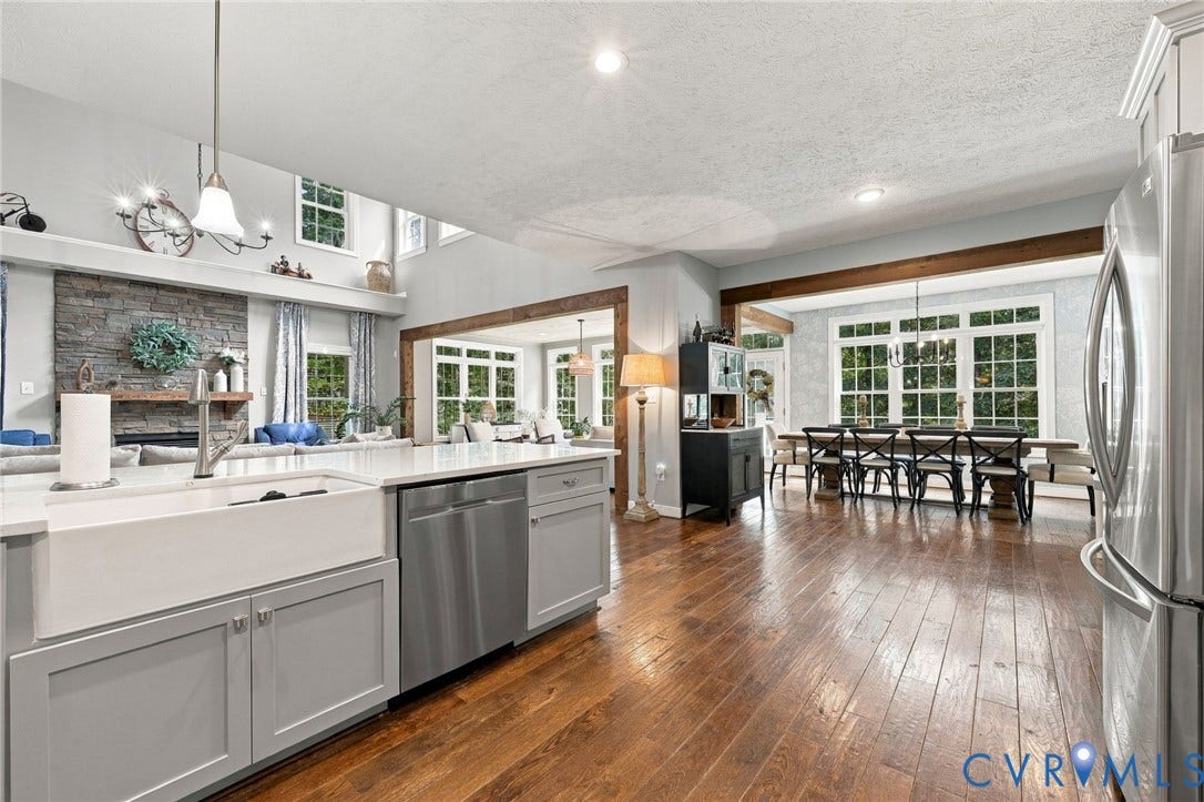 8301 Macandrew Terrace, Chesterfield, VA 23838 Open-concept living area featuring wood-finish flooring, a stone-faced fireplace with a mantel, a farmhouse sink, stainless steel appliances, and exposed wood beams