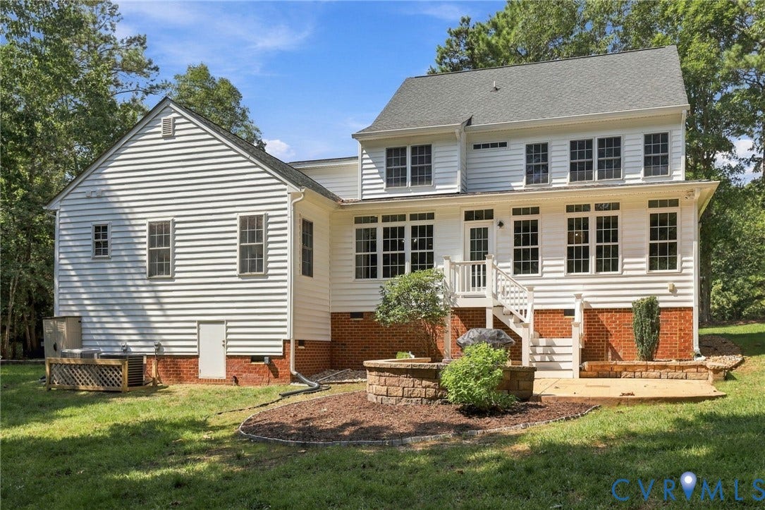 8301 Macandrew Terrace, Chesterfield, VA 23838 Rear exterior featuring white siding, a multi-pane window array, and a stone-accented patio with a built-in fire pit