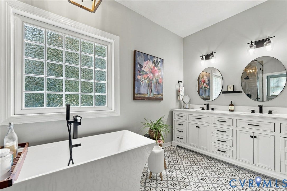8301 Macandrew Terrace, Chesterfield, VA 23838 Freestanding soaking tub with a floor-mounted matte black faucet, frosted glass block window, double vanity with white cabinetry, dual undermount sinks, and patterned floor tile