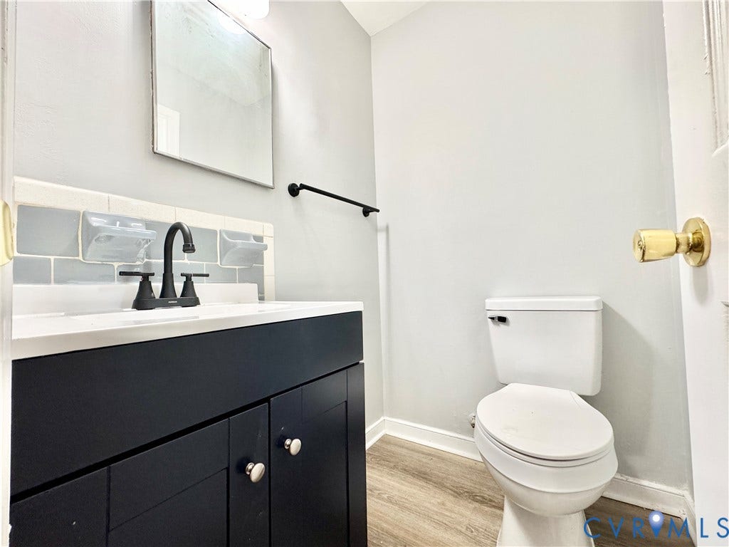 2711 Cheatham Street, Henderson & Johnson, Richmond, VA 23234 Vanity with a white countertop and matte black faucet, subway tile backsplash, rectangular mirror, and wood-finish flooring