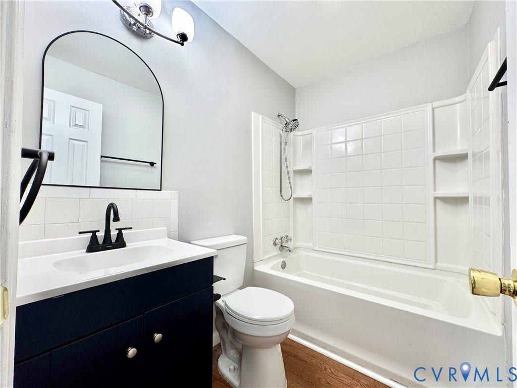2711 Cheatham Street, Henderson & Johnson, Richmond, VA 23234 Bathroom featuring a dark wood-finish vanity, white countertop, modern black fixtures, arched mirror, and a full bathtub with tile-style surround
