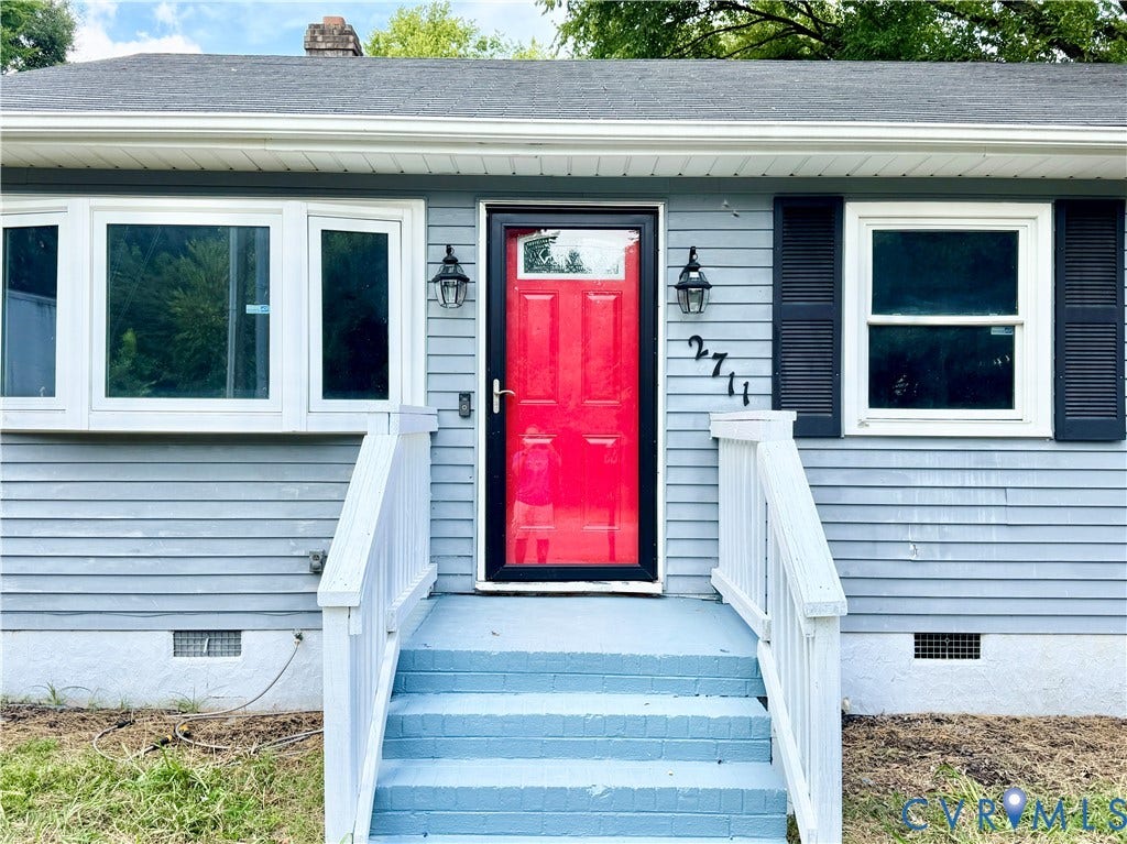 2711 Cheatham Street, Henderson & Johnson, Richmond, VA 23234 Light blue siding with white trim, a vibrant red entry door, bay window, black louvered shutters, and dual exterior wall lanterns